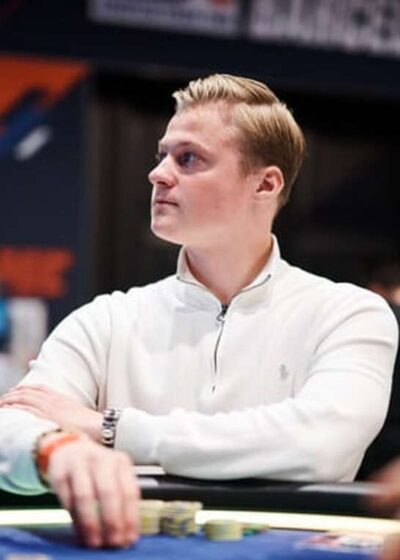 Casimir Seire istuu pokeripöydässä. Hän katsoo sivulle ja pitää kädessään pelimerkkejä. Seirellä on päällään valkoinen paita.