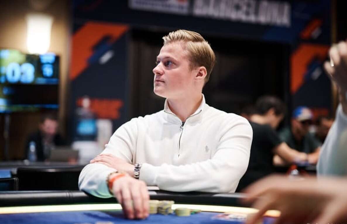 Casimir Seire istuu pokeripöydässä. Hän katsoo sivulle ja pitää kädessään pelimerkkejä. Seirellä on päällään valkoinen paita.