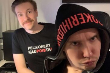 Mies huppu päässä ja duckface naamalla, takana toinen hymyilee paidassa jossa lukee "pelikoneet pois kaupoista"