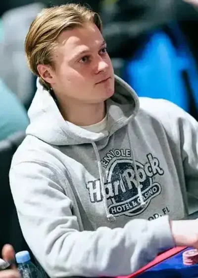 Casimir Seire istuu pokeripöydässä päällään harmaa huppari. Hän katsoo mietteliäänä sivulle ja nojaa kädellään pelipöytään.