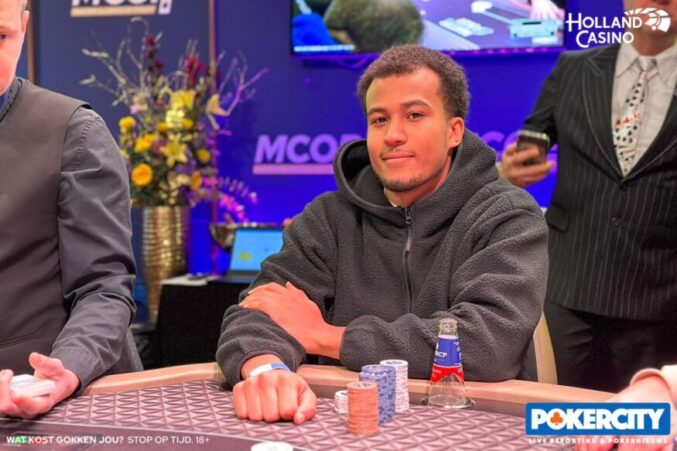 Mies istuu pokeripöydän ääressä edessään merkkipino ja päällään harmaa huppari