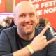 Markus "Muuvipeikko" Ylänne istuu pokeripöydässä ja hymyilee aika leveästi. Ylänne pitää paria sormea pystyssä hevimäisesti.