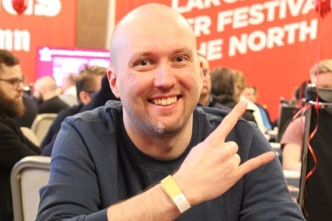 Markus "Muuvipeikko" Ylänne istuu pokeripöydässä ja hymyilee aika leveästi. Ylänne pitää paria sormea pystyssä hevimäisesti.