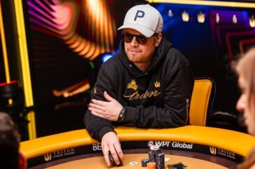Joni Jouhkimainen istuu Triton Poker Serieksessä pokeripöydässä. Hänellä on päällään musta huppari sekä valkoinen Peakin lippis.