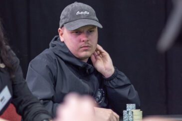 Elias Suhonen istuu mietteliäänä pokeripöydässä. Hän nojaa vasemmalla kädellään leukaan.Hänellä on päässään musta lippis.