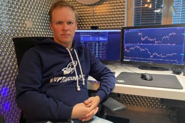 Mikko Rahtu istuu työtuolissaan sininen huppari päällään. Takana on tietokoneen näyttöjä, jotka ovat täynnä erilaisia graafeja.