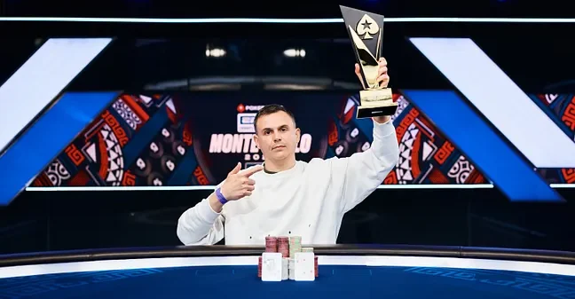 Aleksandr Shevliakov istuu EPT Monte Carlon jälkeen voittajakuvassa. Kädessään hänellä on voittopokaali ja edessään voittokäsi.