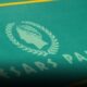 Pokeripöytä on vihreä ja siinä on Caesars Palacen logo, joka on kultaisen värinen ja sen ylä sekä alapuolella on keltainen viiva.