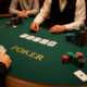 Pokeripöydässä istuu jakaja ja pelaajia. Pelaajilla on edessään eri kokoisia pelimerkkipinoja. Jakajalla on valkoinen paita.