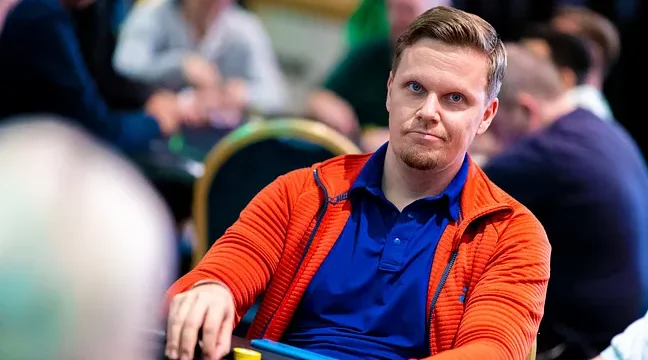 Joni Liimatta istuu pokeripöydässä. Hänellä on edessään pelimerkkejä. Jonilla on päällään punainen huppari, jonka alla t-paita