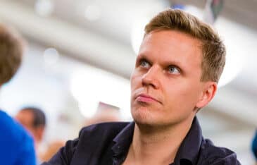 Mies katsoo vasemmalle. Hänellä on lyhyet hiukset ja musta kauluspaita. Vieressä näkyy sinipaitainen mies. Tausta on vaaleaa.