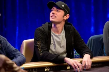 Tom Dwan istuu pokeripöydässä Triton Poker Serieksen turnauksessa. Hänellä on päällään huppari, joka on auki ja musta lippis.