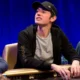 Tom Dwan istuu pokeripöydässä Triton Poker Serieksen turnauksessa. Hänellä on päällään huppari, joka on auki ja musta lippis.