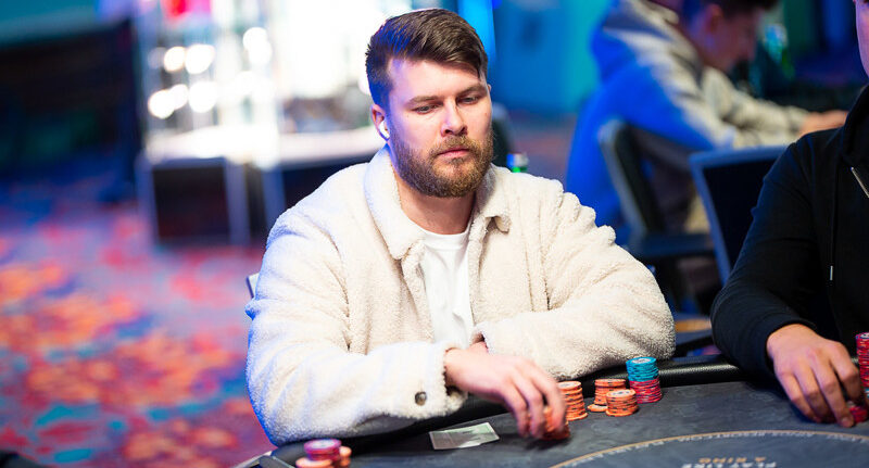 Toni Kaukua istuu pokeripöydässä. Hänellä on päällään valkoinen takki. Edessään pöydällä hänellä on erivärisiä pelimerkkejä.
