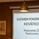 Valkokankaalla lukee Suomen pokerinpelaajat ry kevätkokous. Vasemmalla puolella on ruskeaa seinää, jossa on muutamia tauluja.