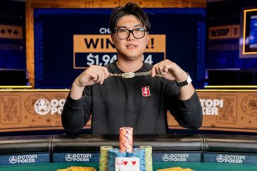 Mies istuu pokeripöydässä. Hänellä on päällään musta paita. Käsissään hän pitää kultaista ranneketta. Tausta on vaalean ruskeaa.
