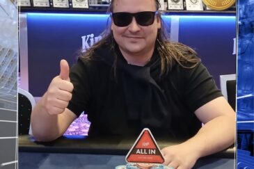 Pitkähiuksinen mies istuu pokeripöydässä. Hänellä on päällään musta t-paita sekä mustat aurinkolasit. Hän näyttää myös peukkua.