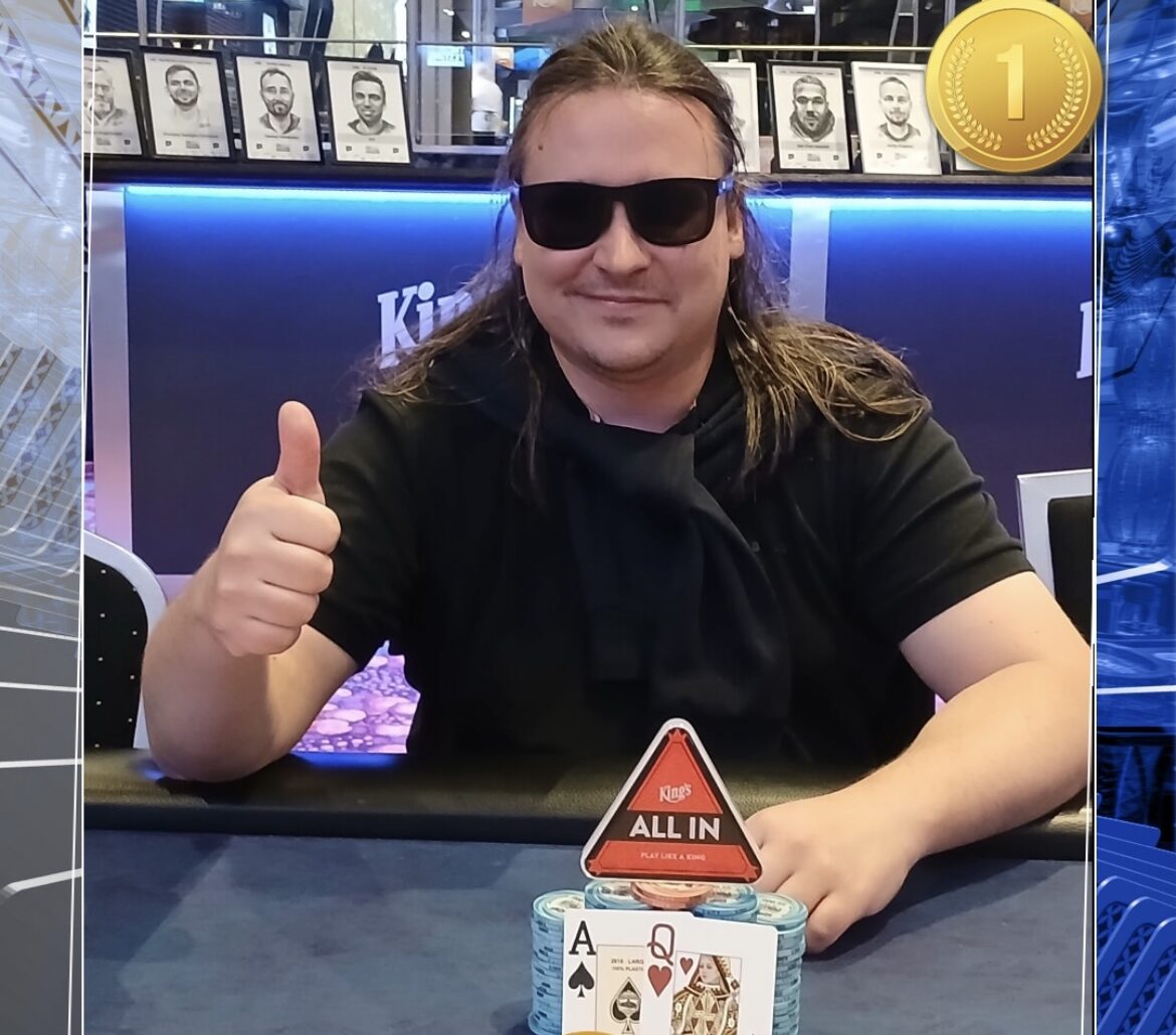 Pitkähiuksinen mies istuu pokeripöydässä. Hänellä on päällään musta t-paita sekä mustat aurinkolasit. Hän näyttää myös peukkua.
