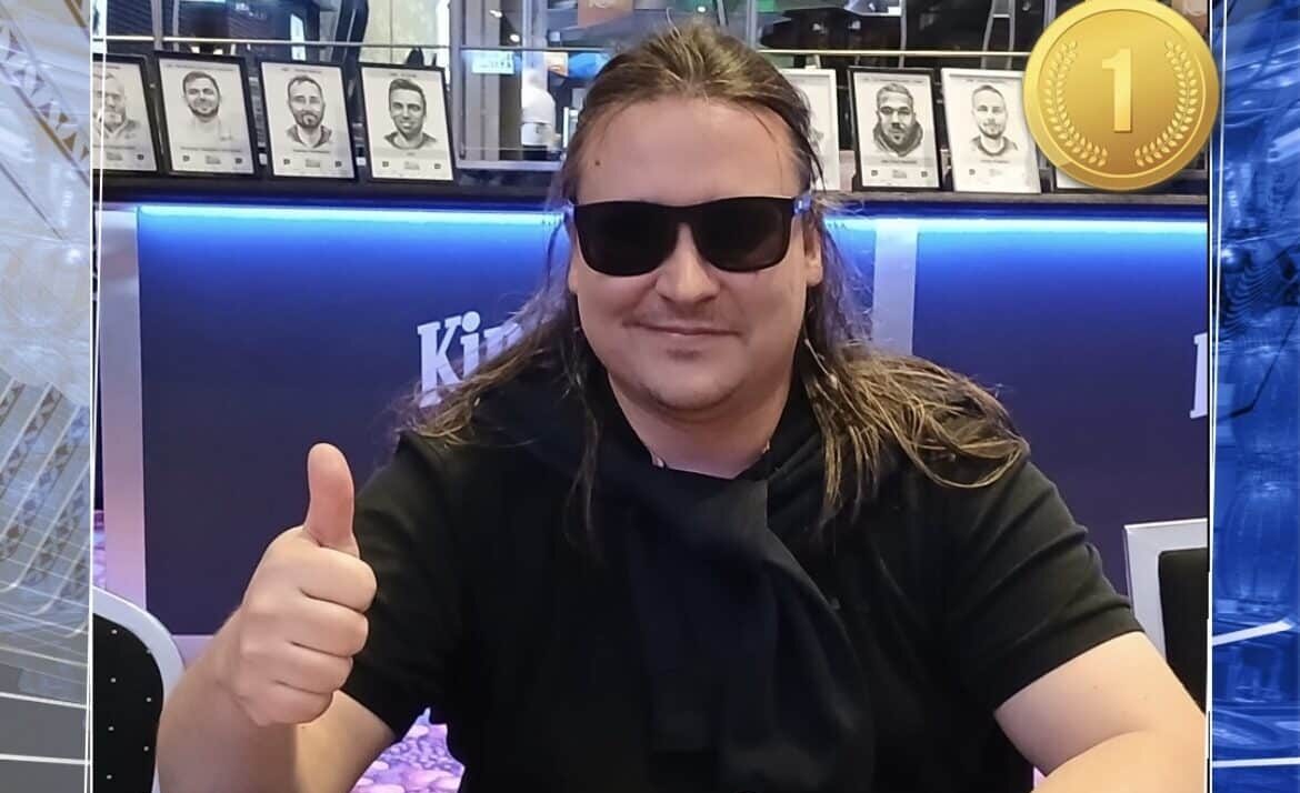 Pitkähiuksinen mies istuu pokeripöydässä. Hänellä on päällään musta t-paita sekä mustat aurinkolasit. Hän näyttää myös peukkua.