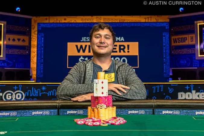 Mies istuu pokeripöydässä päällään harmaa huppari. Hän hymyilee ja hänen edessään on keltaisia ja pinkkejä pelimerkkejä.