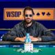 Mies istuu pokeripöydässä ja hymyilee. Hänellä on päällään musta takki ja päässään aurinkolasit. Kauempana taustalla lukee WSOP.