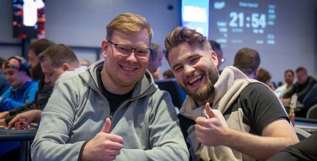 Kuvassa on kaksi iloista miestä, toisella on harmaa paita, ja toisella vaalea paita. Taustalla näkyy sinisellä näytöllä ajastin.