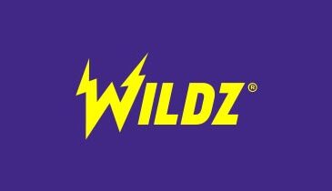 Edessä on nettikasino Wildzin logo. Logo on väriltään keltainen. Tausta on Wildzin brändin mukaisesti vaalean violettia.