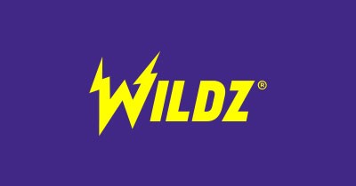 Edessä on nettikasino Wildzin logo. Logo on väriltään keltainen. Tausta on Wildzin brändin mukaisesti vaalean violettia.