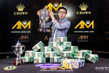 Pokeripöydällä on valtava määrä rahaa, pokaali ja pelikortteja. Pöydän takana seisoo mies, joka pitää toista pokaalia kädessään.