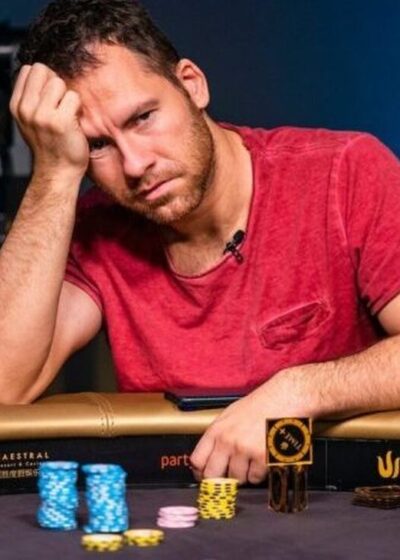 Mies istuu pokeripöydässä päällään punainen paita. Hän nojaa kädellään päähänsä ja hänen ilme on mietteliäs. Pöydällä on pelimerkkejä.