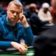 Mies istuu pokeripöydässä. Hänellä on mietteliäs ilme ja hän nojaa käteensä. Miehellä on toisessa kädessään pelimerkkejä.