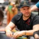 Mies istuu pokeripöydässä. Hänellä on päällään musta t-paita ja musta lippis. Miehen kädet on vihreällä pöydällä.