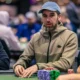 Miehet istuu pokeripöydässä. Heillä on edessään pelimerkkejä. Kahdella miehistä on päässään lippikset. Takana näkyy lisää ihmisiä.