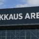 Kuvassa näkyy rakennusken seinää. Seinässä lukee mustalla pohjalla Veikkaus Arena. Taustalla näkyy sinivalkoinen taivas.