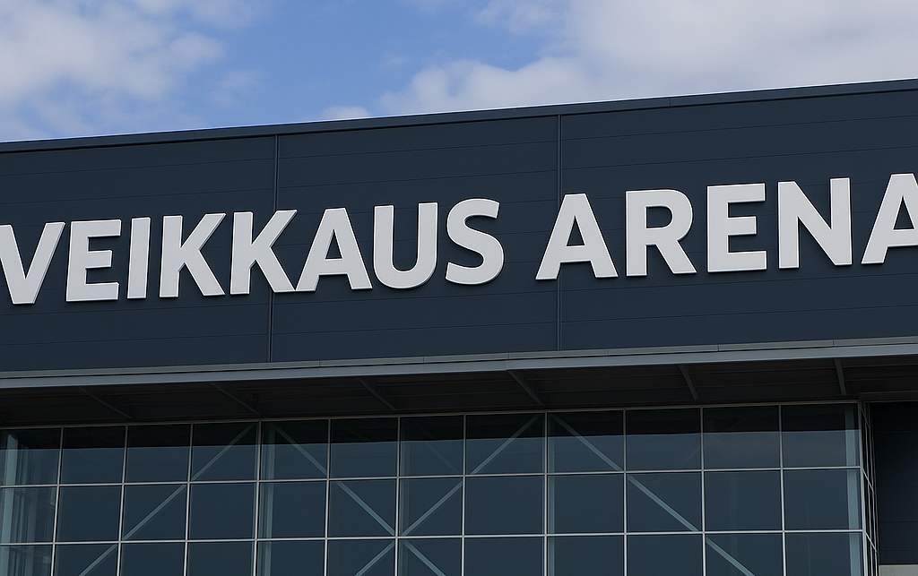 Kuvassa näkyy rakennusken seinää. Seinässä lukee mustalla pohjalla Veikkaus Arena. Taustalla näkyy sinivalkoinen taivas.