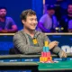 Mies istuu pokeripöydässä ja hymyilee. Hänen edessään pöydällä on erivärisiä pelimerkkejä torneissa. Takana näkyy ihmisiä.