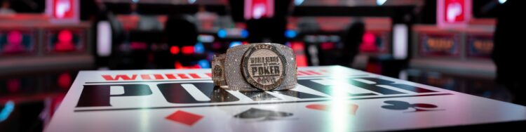 Pöydässä lukee World Series of Poker. Pöydän päällä on kiiltelevä ranneke, jossa on paljon timantteja. Takana näkyy pokeripöytä.
