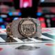 Pöydässä lukee World Series of Poker. Pöydän päällä on kiiltelevä ranneke, jossa on paljon timantteja. Takana näkyy pokeripöytä.