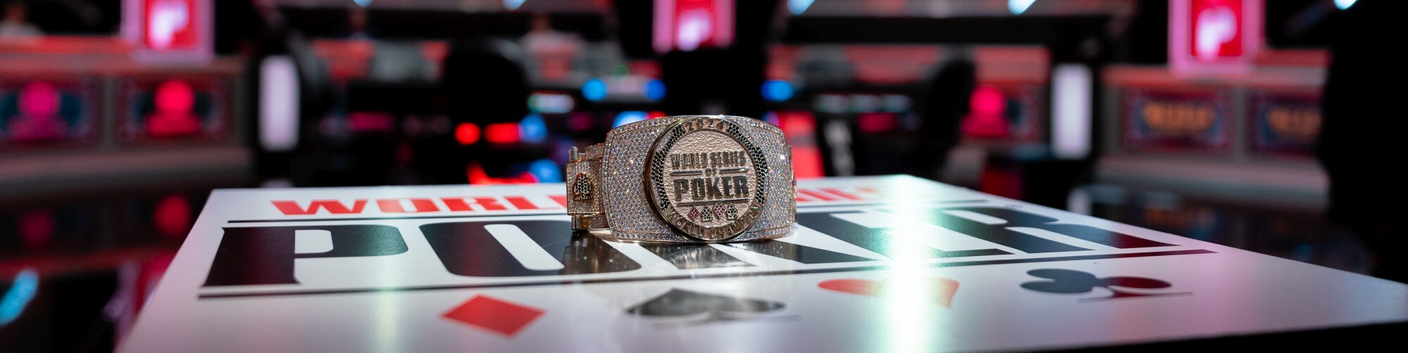 Pöydässä lukee World Series of Poker. Pöydän päällä on kiiltelevä ranneke, jossa on paljon timantteja. Takana näkyy pokeripöytä.