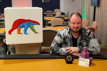 Antti Nieminen istuu oranssin pelipöydän ääressä edessään pytty ja merkkejä, Vieressä on Coolbetin mainostaulu, jossa on värikäs jääkarhu.