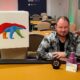 Antti Nieminen istuu oranssin pelipöydän ääressä edessään pytty ja merkkejä, Vieressä on Coolbetin mainostaulu, jossa on värikäs jääkarhu.