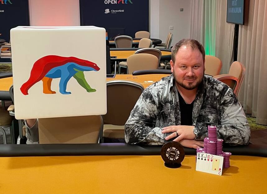 Antti Nieminen istuu oranssin pelipöydän ääressä edessään pytty ja merkkejä, Vieressä on Coolbetin mainostaulu, jossa on värikäs jääkarhu.