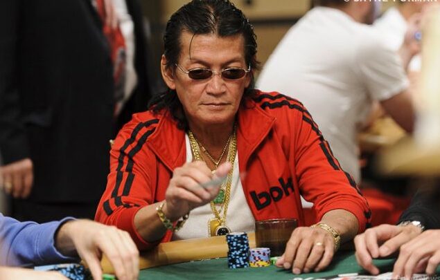 Scotty Nguyen istuu pokeripöydän ääressä punaisessa takissa ja aurinkolasit päässään edessään merkkipino