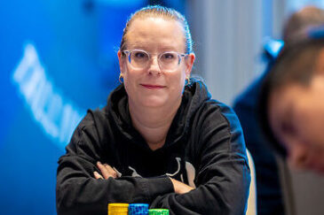 Nainen, jolla on silmälasit istuu pokeripöydän ääressä mustassa hupparissa. Tausta on sininen ja valkoinen, etualalla näkyy mies.