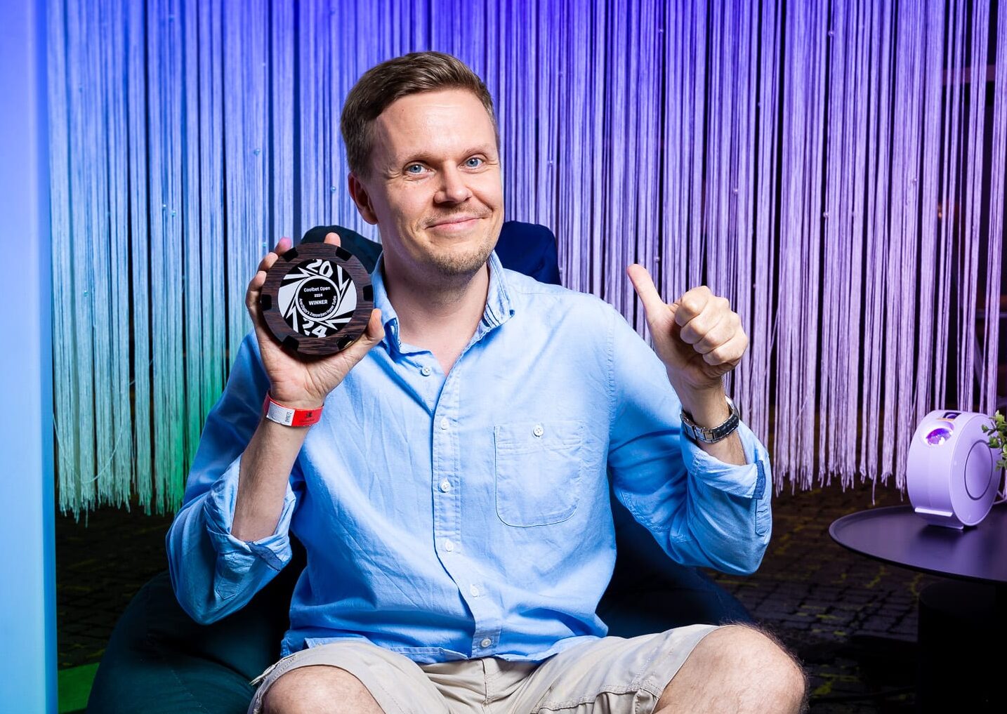 Mies pitää kädessään pokaalia ja näyttää peukkua. Hänellä on päällään sininen kauluspaita.