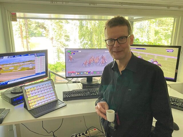 Jorma Vuoksenmaa kotitoimistollaan kahvikuppi kädessä mustassa kauluspaidassa.