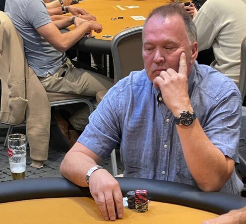 Keimo Suominen istuu pokeripöydän ääressä sinisessä paidassa ja nojaileen käteensä mietiskelevän näköisenä.