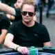 Mies istuu pokeripöydässä. Hänellä on päällään musta t-paita ja mustat aurinkolasit. Miehen edessä pöydällä on pelimerkkejä.
