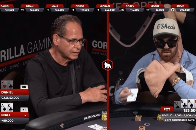 Kaksi silmälasipäistä miestä istuvat pokeripöydässä. Toisella on musta paita ja toisella sininen paita ja lippalakki päässään.