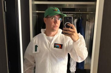 Miehellä on valkoinen haalari päällä jossa on merkkejä rinnassa ja vihreä lippalakki.